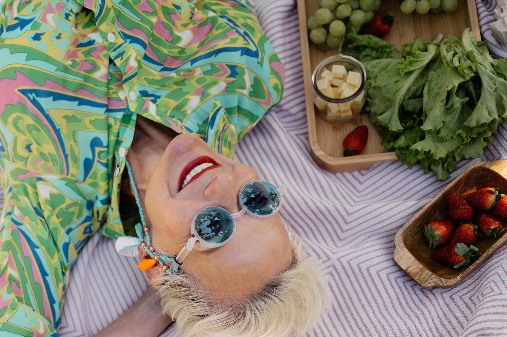 A woman over 40 lays happily on a picnic blanket with her eyes to the sky.